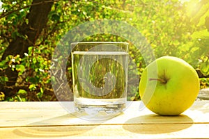 A glass of water and a green apple early in the morning on a natural background. The concept of morning, healthy food and diet.