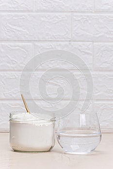 Glass of water and a jar of collagen goodnesson a marble beige background