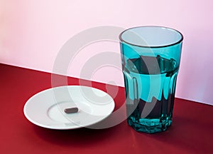 Glass of water and medical pills on a white plate on a red and pink background