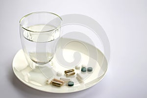 Glass of water and pills on a plate isolated on white. Medicine and health concept