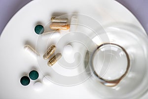 Glass of water and pills on a plate isolated on white. Medicine and health concept