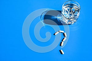 Glass of water and pills in shape of question mark on blue background. Hard light and shadows. Vitamins and prebiotics, probiotics photo