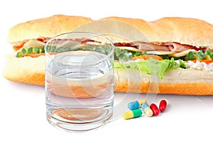 Glass of water, pills and two hot dogs with various ingredients.