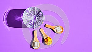 Glass of water and pills on wooden spoon on purple background with hard light and shadows. Creative. Vitamins and prebiotics,