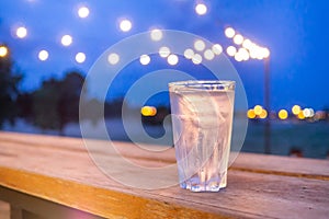 A glass of water placed on a wooden table with beautiful lighting at night with dark blue sky backgrounds