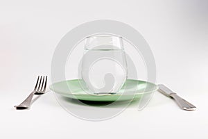 Glass of water in a plate with knife and fork isolated on white