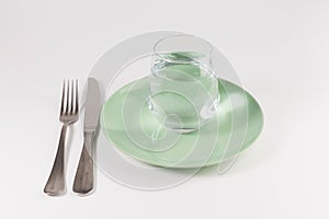 Glass of water in a plate with knife and fork isolated on white