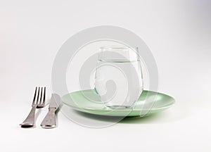 Glass of water in a plate with knife and fork isolated on white