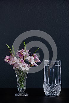 A glass of water and purple flowers in a vase placed on the table
