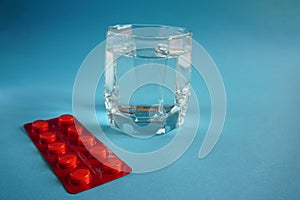 Glass of water with red plate of pills on blue background