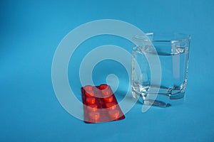 Glass of water with red plate of pills on blue background