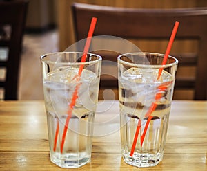 Glass of water with red straw on wooden table