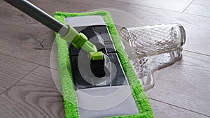 a glass of water spilled on the laminate floor, a mop wipes the water