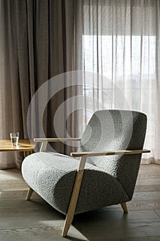 Glass of water standing on wooden table near grey armchair