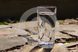 A glass of water stands on a gray broken paving slab