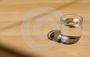 A glass of water on top of wooden table. Glass water and sunlight