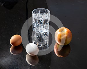 Glass of water with two eggs placed beside it on a dark background.