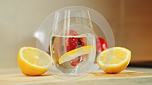 A glass with water between two part of cut lemon on wooden kitchen board