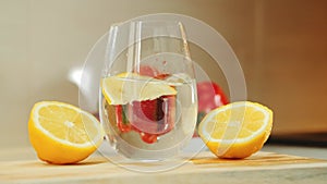 A glass with water between two part of cut lemon on wooden kitchen board