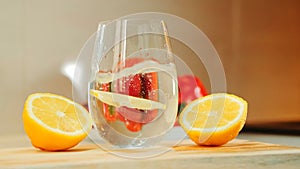 A glass with water between two part of cut lemon on wooden kitchen board