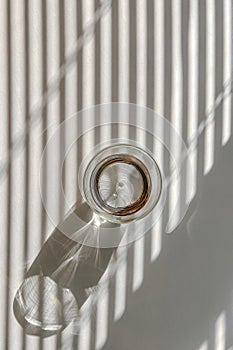 Glass of water on the white table with shadows from the morning light throught the blinds