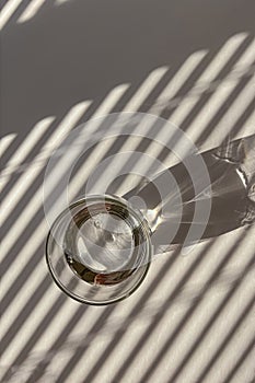 Glass of water on the white table with shadows from the morning light throught the blinds