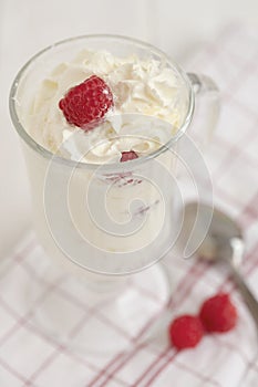 Glass with whipped cream and raspberries on a checkered napkin