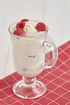 Glass with whipped cream and raspberries on a checkered napkin