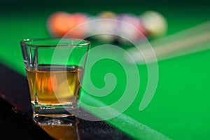 Glass of whiskey on billiard table and billiard balls in background