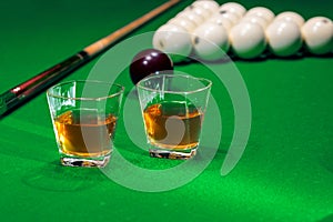 Glass of whiskey on billiard table with cue and billiard balls in background