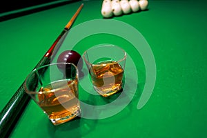 Glass of whiskey on billiard table with cue and billiard balls in background