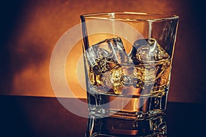 Glass of whiskey on black table with reflection and gold background, warm atmosphere