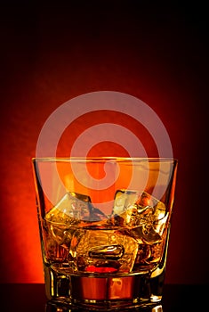 Glass of whiskey on black table with reflection, red tint atmosphere