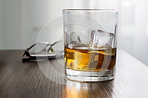 Glass of whiskey, brandy, cognac with ice cubes on wooden table desk with glassess. Mockup of product, gift for man