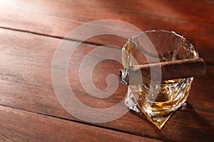 Glass of whiskey and burnt cigar on wooden table, above view. Space for text