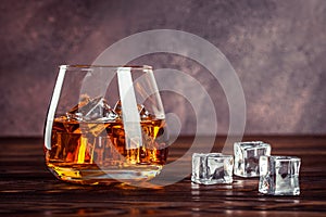 A glass of whiskey close up. Brandy with ice on a brown wooden table. Cognac, bourbon. Strong alcoholic drink. Transparent yellow