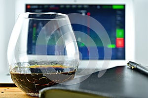 A glass of whiskey in front of a laptop with a stock Ticker on t