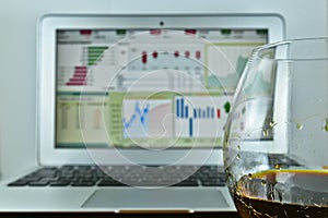 A glass of whiskey in front of a laptop with a stock Ticker on t