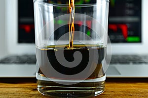 A glass of whiskey in front of a laptop with a stock Ticker on t