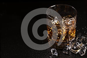 Glass of whiskey with ice on black stone table