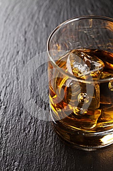 Glass of whiskey with ice on black stone table