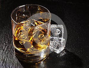 Glass of whiskey with ice on black stone table