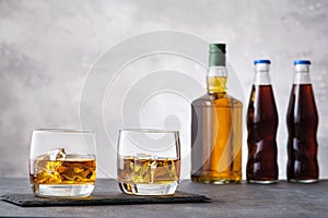 Glass with whiskey and ice cubes on background bottle