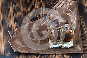 Glass of whiskey and ice cubes on a napkin/Glass of whiskey and ice cubes on a napkin. Wooden table