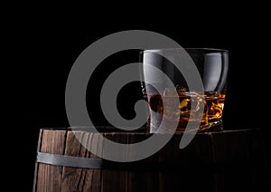Glass of whiskey with ice cubes on top of wooden barrel. Cognac brandy drink