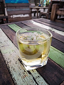 Glass of whiskey with ice cubes on vintage wooden table