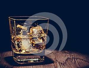 Glass of whiskey with ice cubes on wood table, warm atmosphere, time of relax with whisky