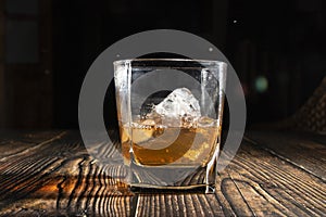 Glass of whiskey with ice cubes on a wooden table. An old tabletop with light and a glass of strong drink.