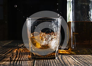 Glass of whiskey with ice cubes on a wooden table. An old tabletop with light and a glass of strong drink.