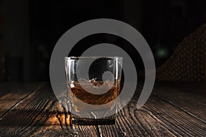 Glass of whiskey with ice cubes on a wooden table. An old tabletop with light and a glass of strong drink.